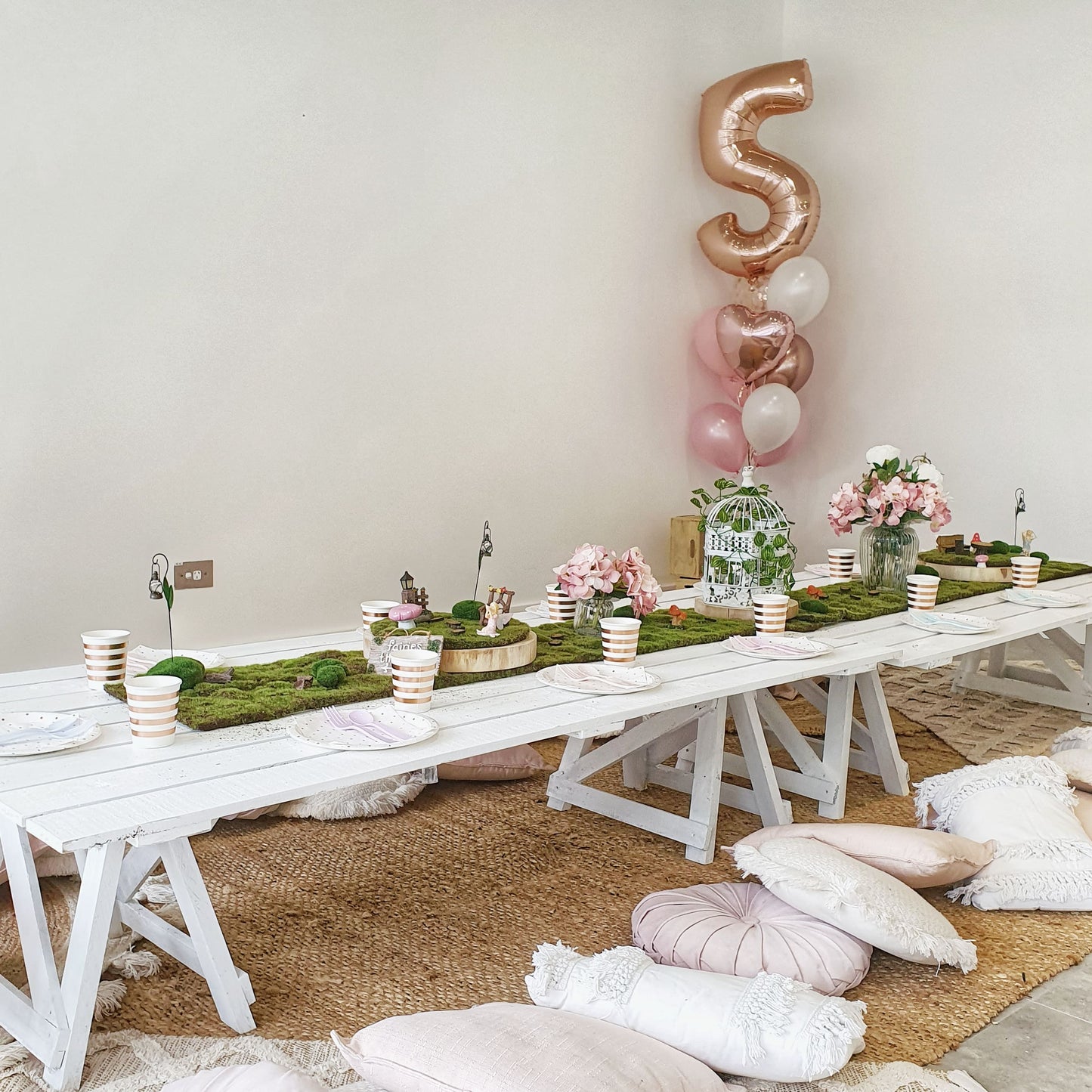 Elegantly styled children's fairy garden party/picnic with helium balloon bouquet and fairy garden table styling, trestle tables, cushions and rugs