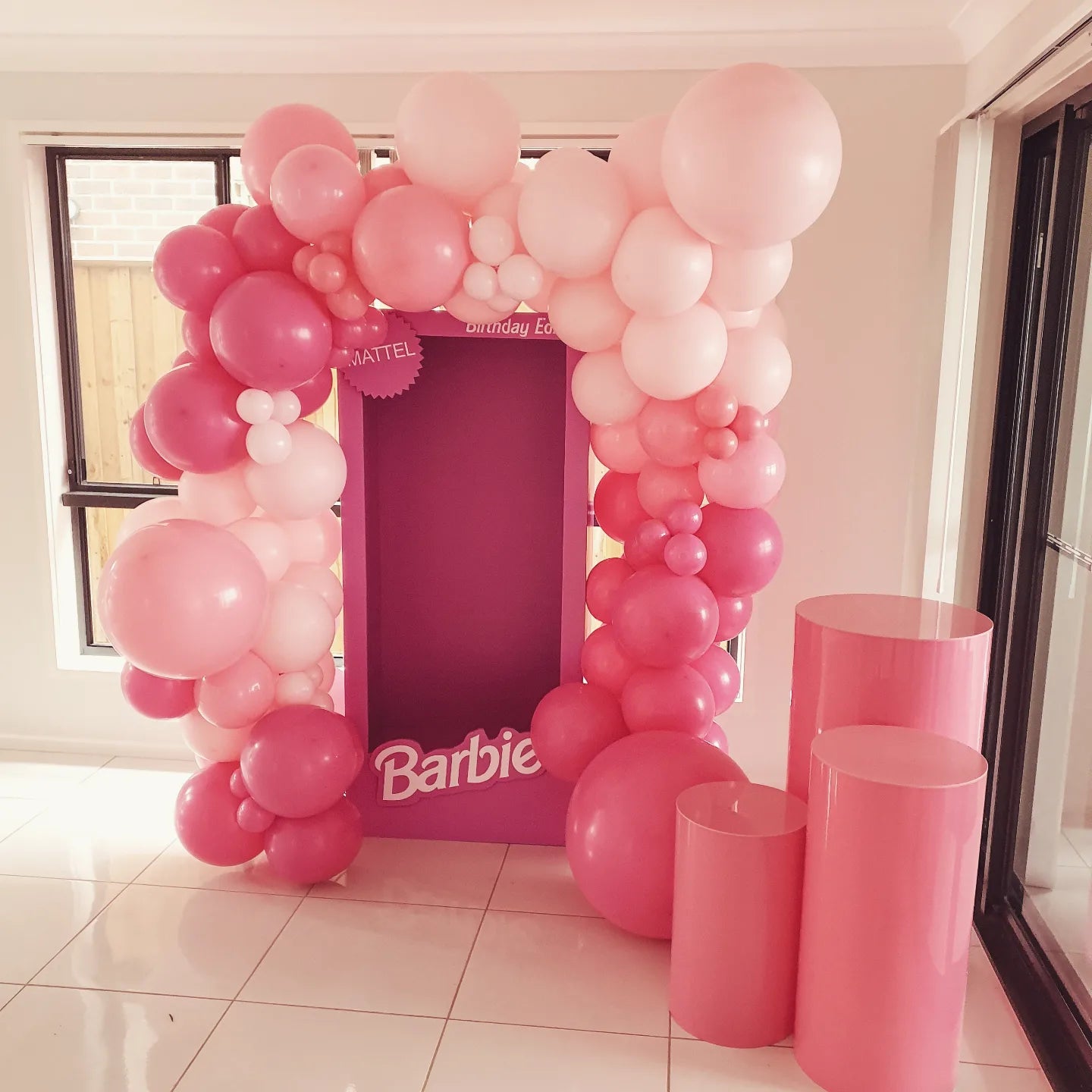 Pink child sized photobooth prop with hot pink acrylic plinths for cake display and an organic balloon garland
