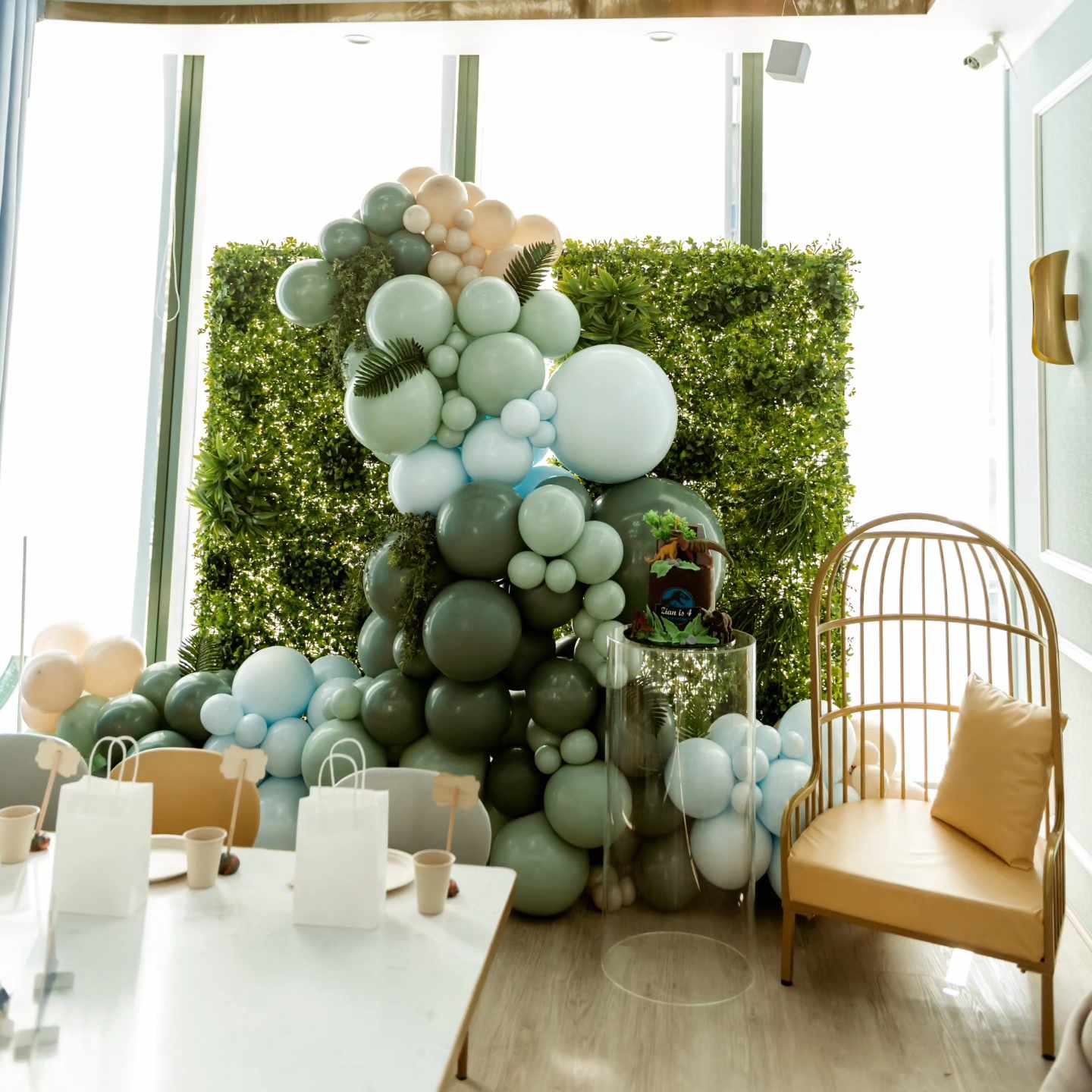 Dinosaur themed birthday party featured our green wall backdrop and organic balloon garland with the dinosaur cake sitting on top of our clear acrylic plinth.