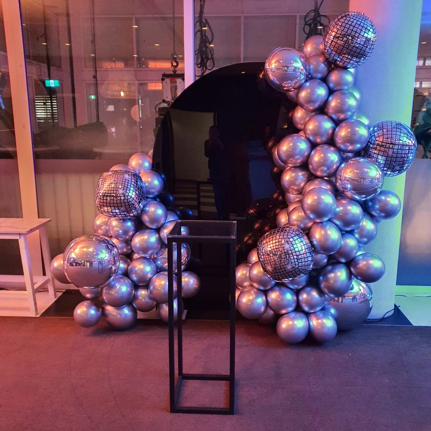 Black sail arch backdrop for a birthday celebration with mirror disco balls in an organic balloon garland decoration with a black steel plinth for the cake display