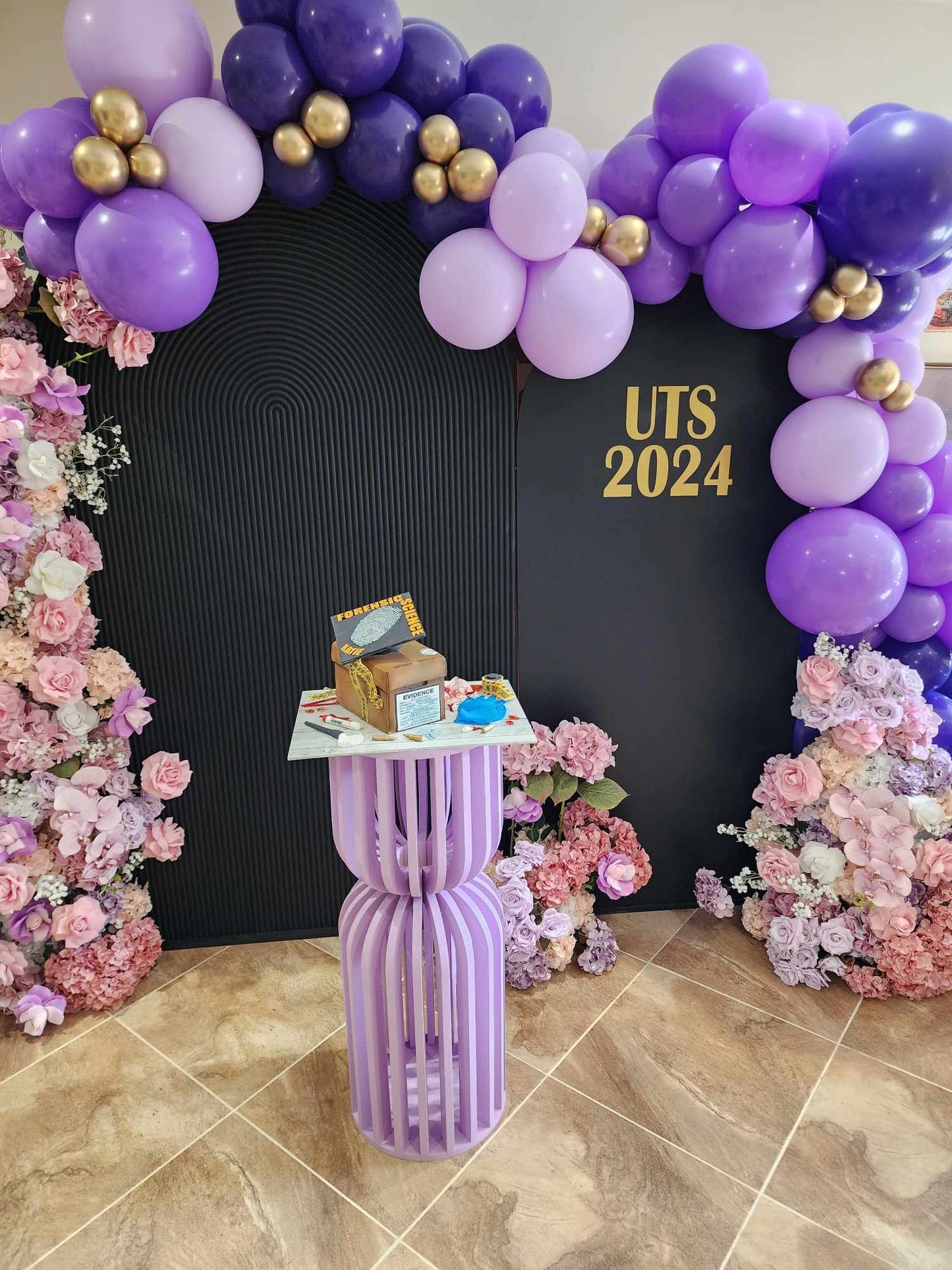 Hour glass plinth painted in a custom purple for a graduation party celebration to display the cake. Also featuring our Ripple arch backdrop in black, balloon garland and faux floral arrangements