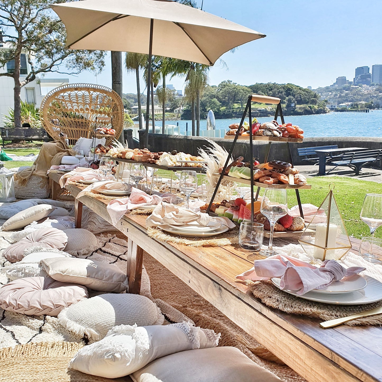 Engagement party pop up picnic setup with comfy cushions, rugs, peacock chair, linen napkins, table styling, umbrellas and grazing board in lavender bay