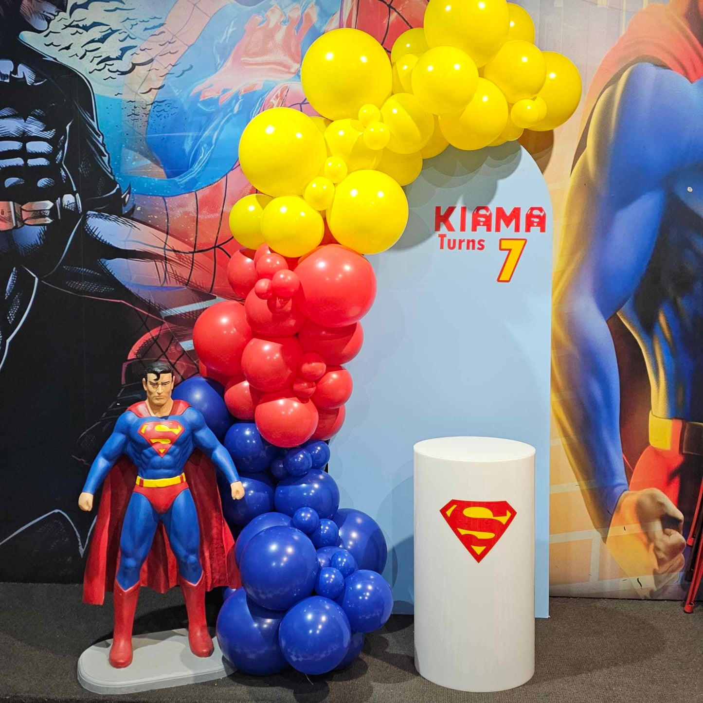 Superman themed birthday party, 3.5m balloon garland with blue arch backdrop, White acrylic plinth with superman personalisation perfect for superhero birthday celebrations at a playcentre.