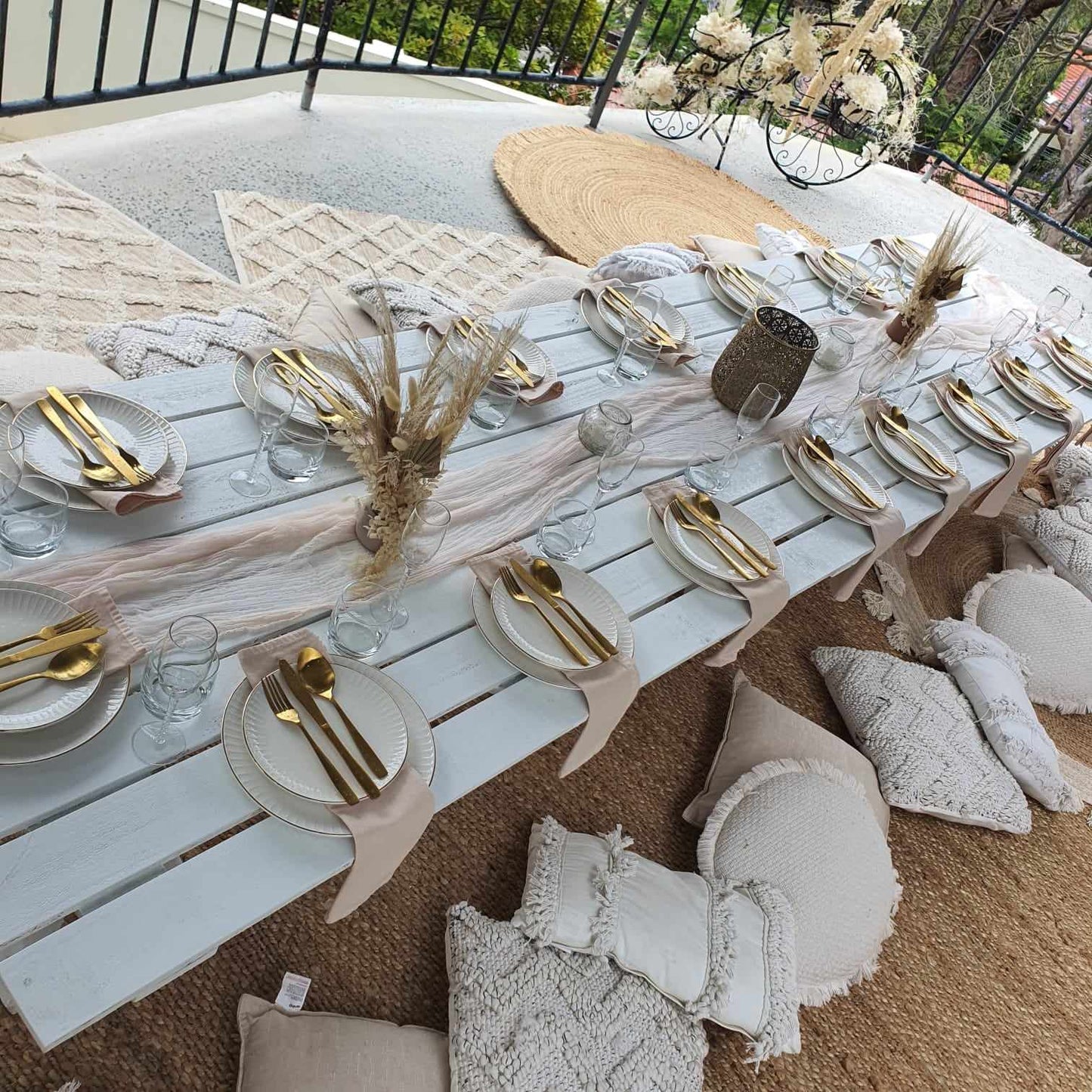 Birthday party pop up picnic setup with comfy cushions, rugs, peacock chair, linen napkins, table styling, and white trestle tables