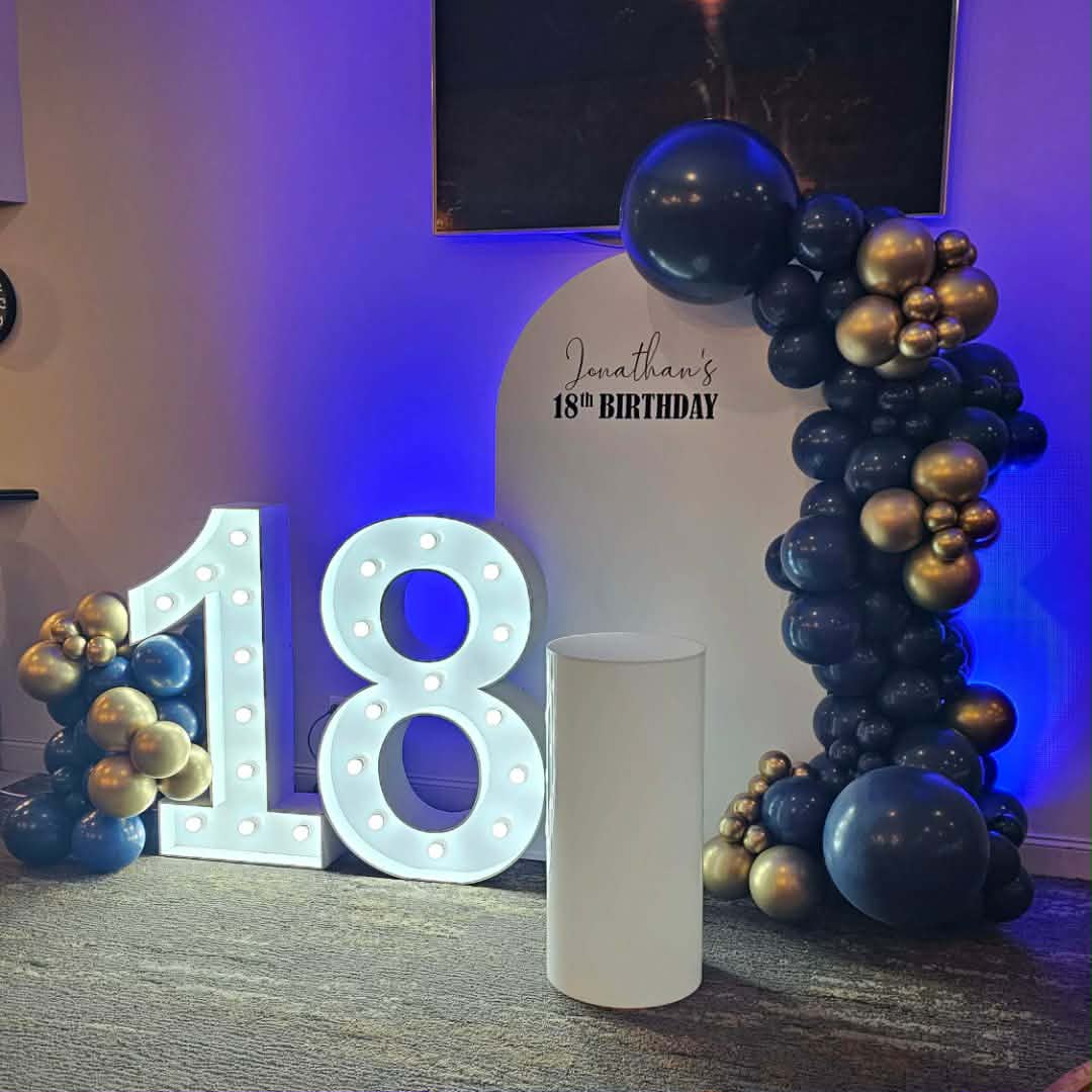 Decorative setup for a 18th birthday party with Navy and Gold Balloon garland, Light up Number 18 and Arch backdrop for a milestone birthday