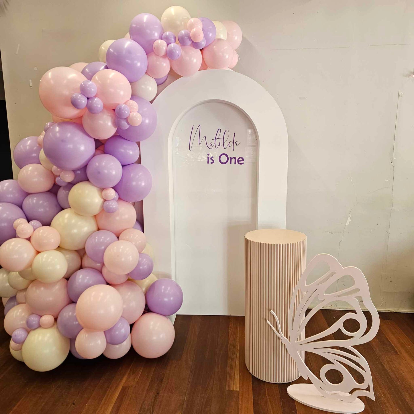 Closed arch backdrop with butterfly prop, ripple plinth and organic balloon garland for a first birthday