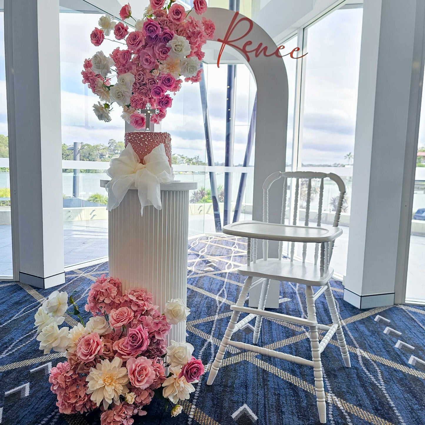 Christening decorations Open arch backdrop, white vintage high chair, White ripple plinth, Faux floral arrangements and Acrylic name sign.