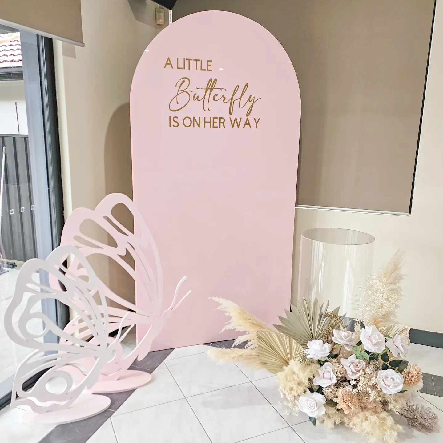 Decorations include a Large pink arch backdrop, Clear acrylic plinth, butterfly props, faux floral arrangement and personalisation for a butterfly themed baby shower, baby sprinkle or first birthday