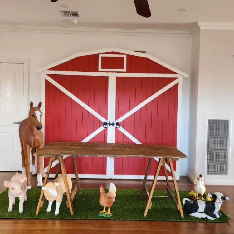 Red Barn door farm yard backdrop. Wooden trestle table and farm animal props for farm themed birthday party decorations. lamb, Calf, piglet, foal chickens and chicks lifesize props 