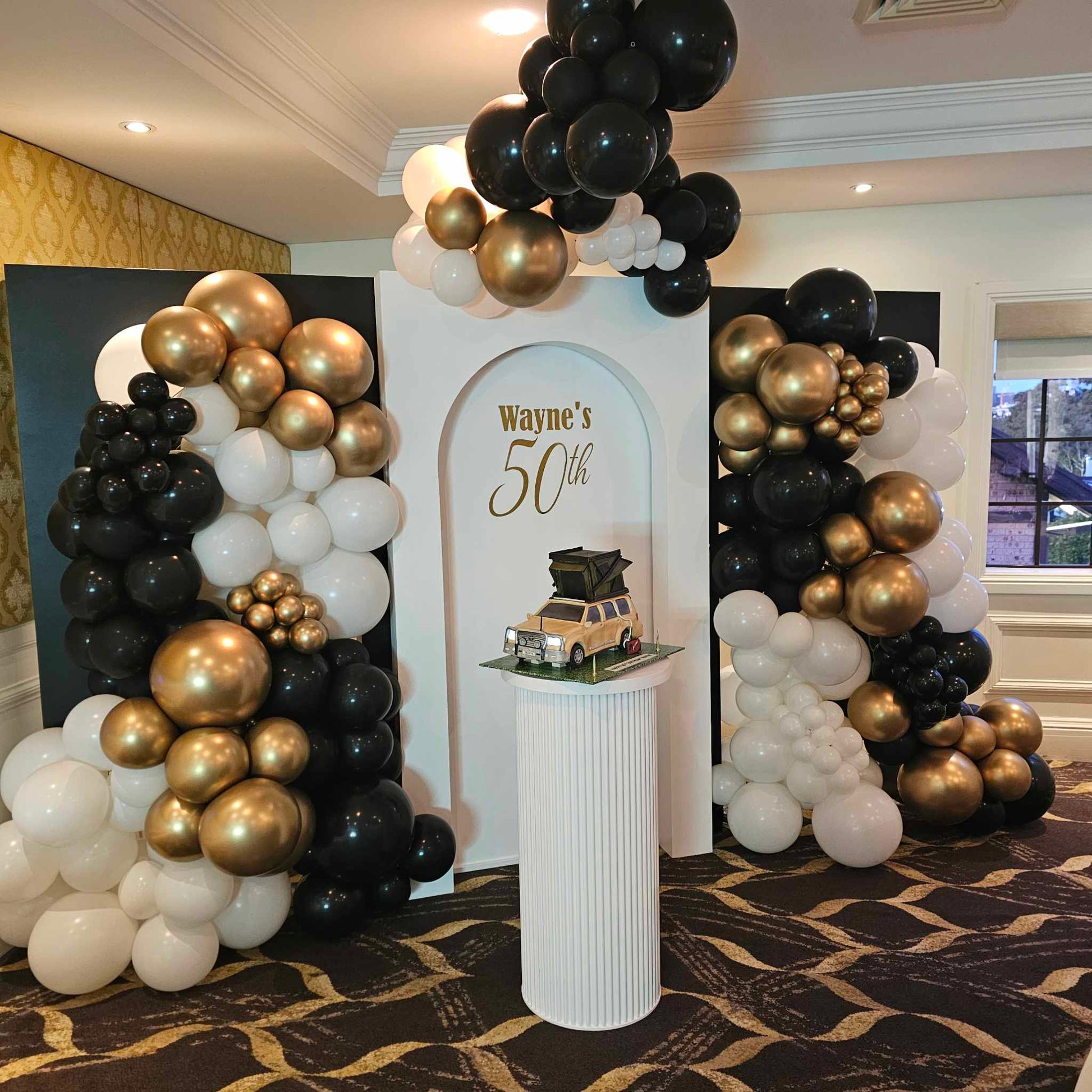 Open and Closed Arch backdrops in black and white pictured with our white ripple plinth displaying the birthday cake, classic black, white and gold balloon garland and personalised signage