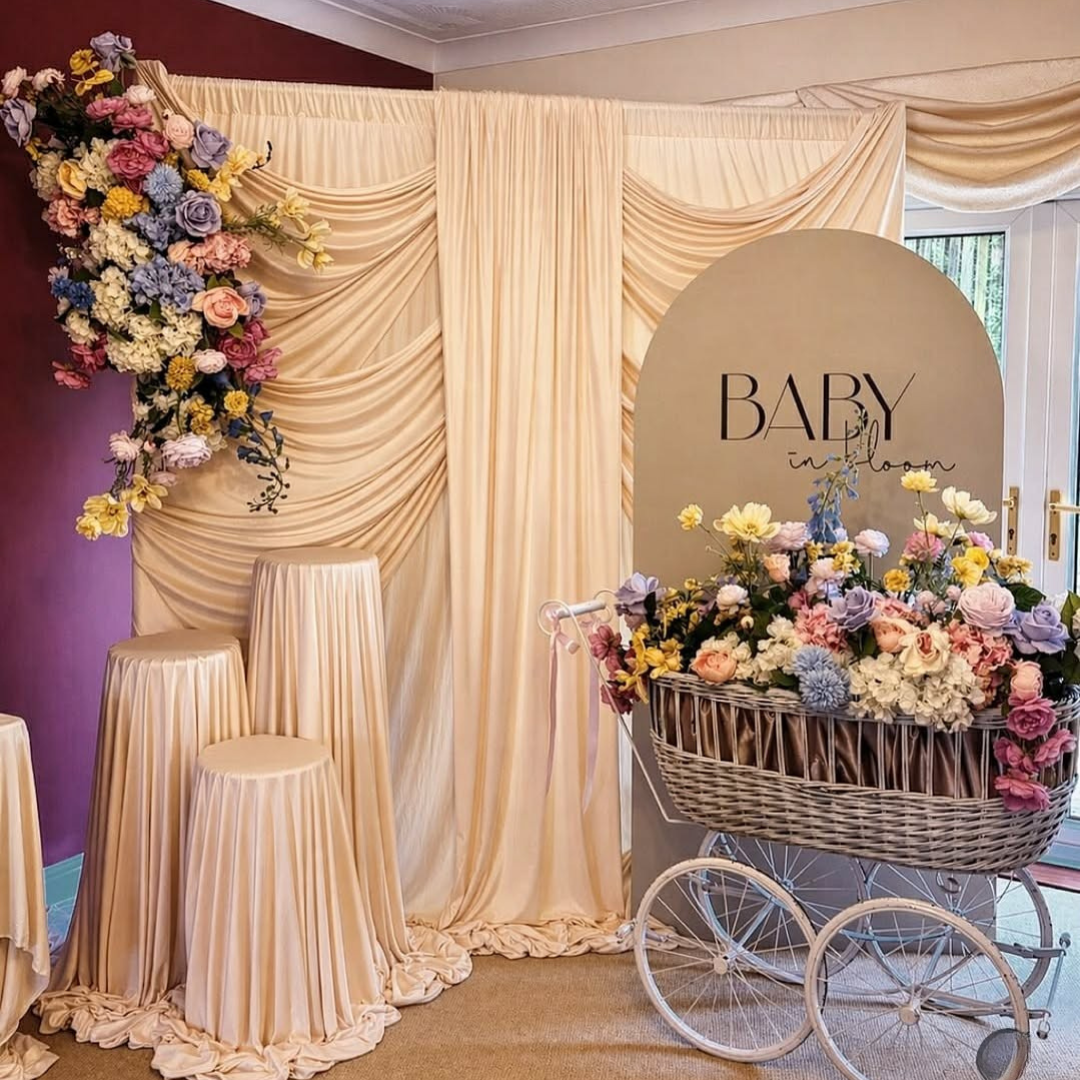 Decorative setup with floral arrangements, draped curtains, and a baby carriage at a baby shower.
