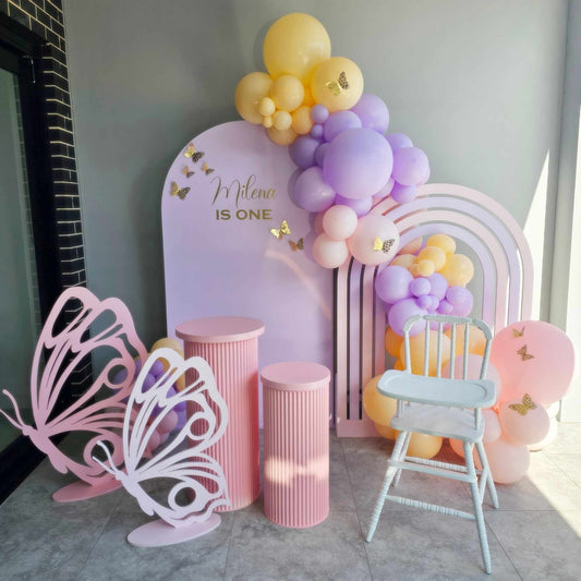 Rainbow arch backdrop in our butterfly package with Pink ripple plinths, Gold paper butterflies, organic balloon garland and vintage high chair hire