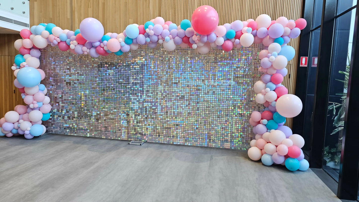 Organic balloon arch with a rainbow shimmer wall backdrop in an indoor setting