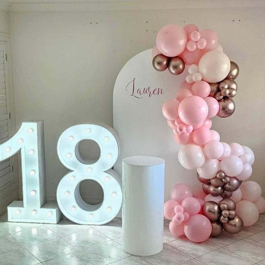 Decorative pink and rose gold balloon garland with Arch backdrop, light up number '18' and personalisation in a room setting.