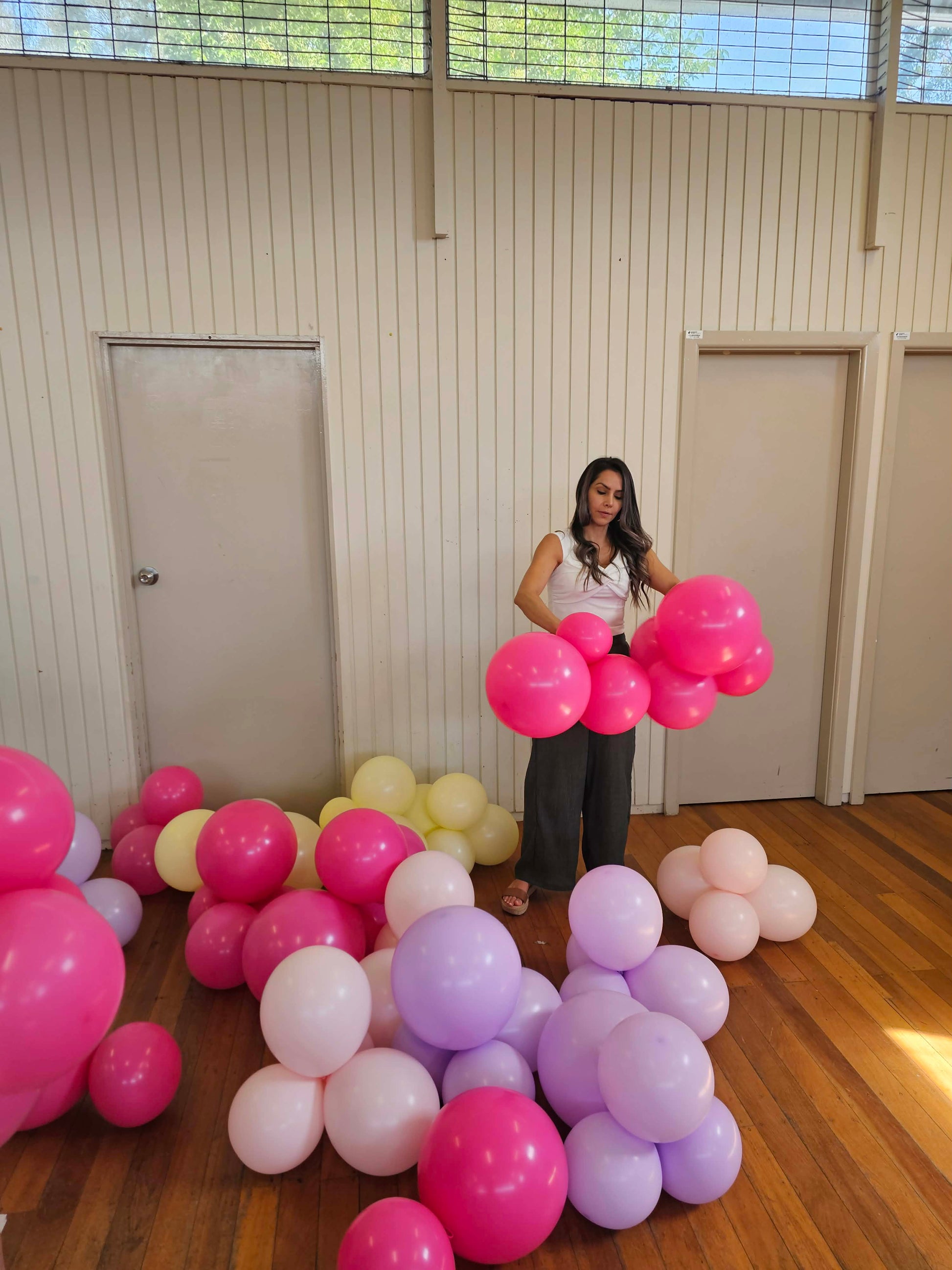 Woman standing amidst pink, purple, and white balloons in a room with wooden floors and white walls. Building an Organic Balloon Garland