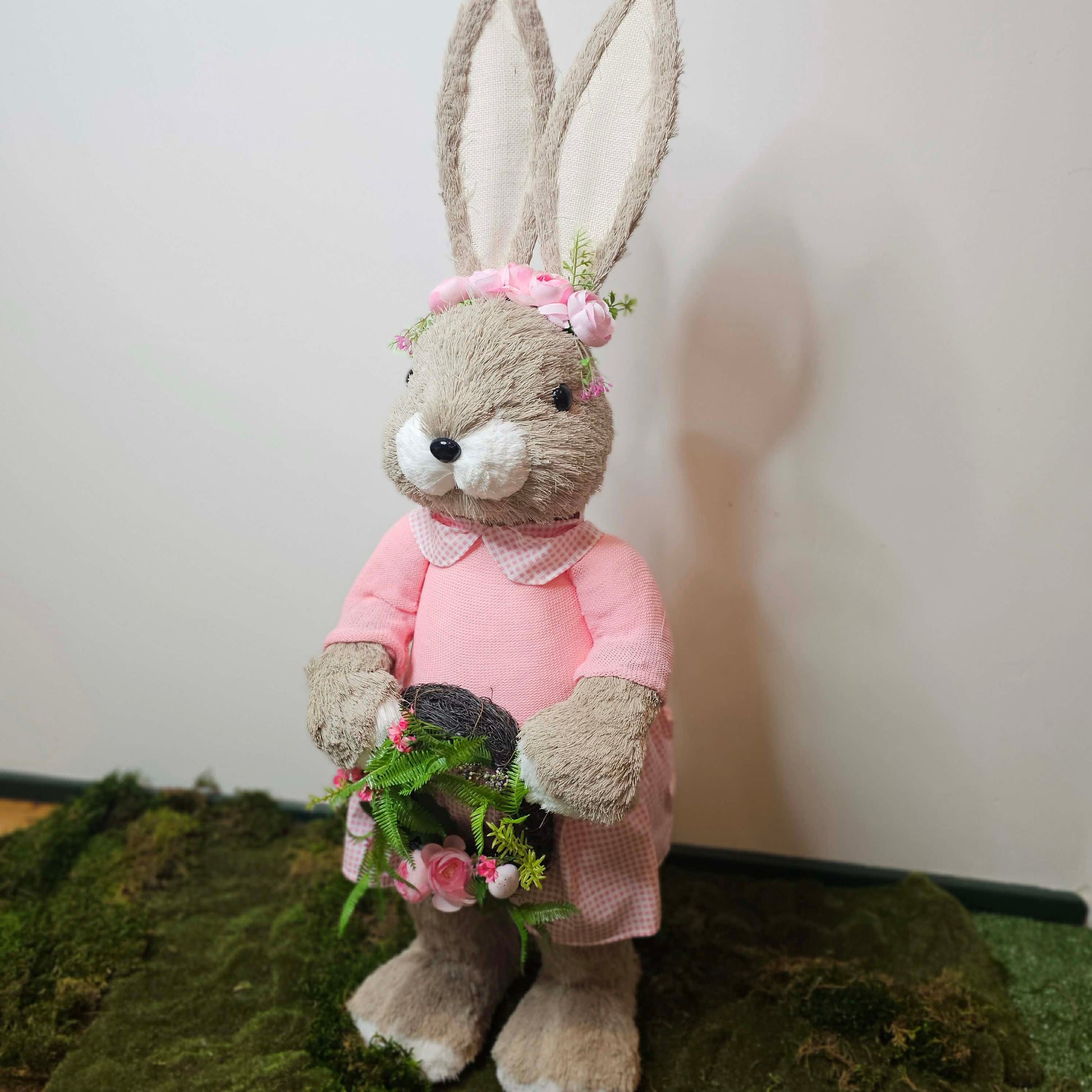 Stuffed bunny in a pink outfit with flowers on a green surface and white background