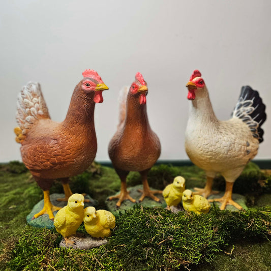 Three resin chickens and chicks on a grassy surface with a plain background
