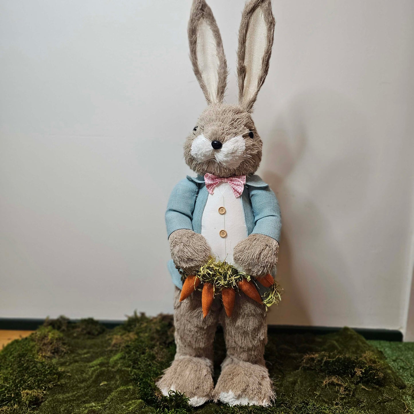 Stuffed bunny holding carrots on a grassy surface with a white background