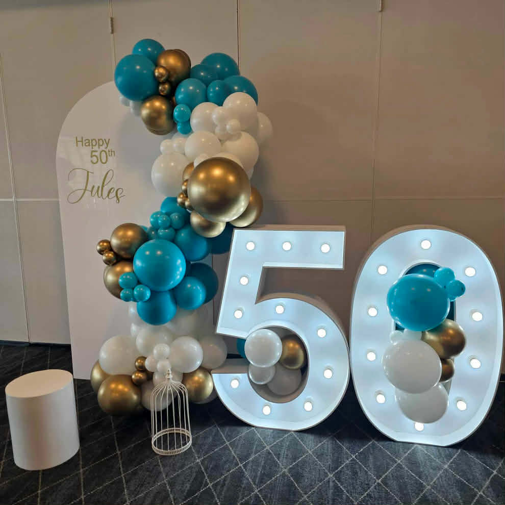 Decorative setup with Arch backdrop balloons and a large light up number '50' for a 50th birthday celebration.